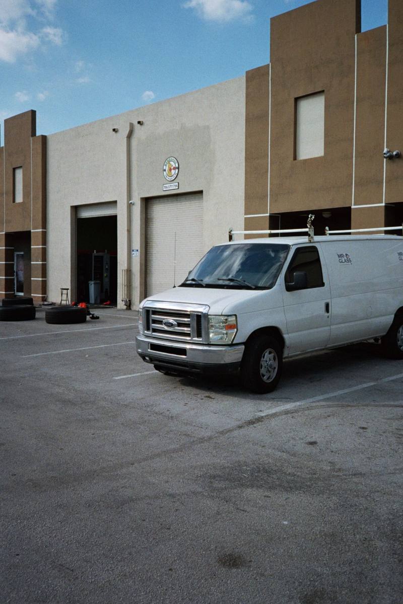 White Ford work van with a ladder rack parked outside a shop